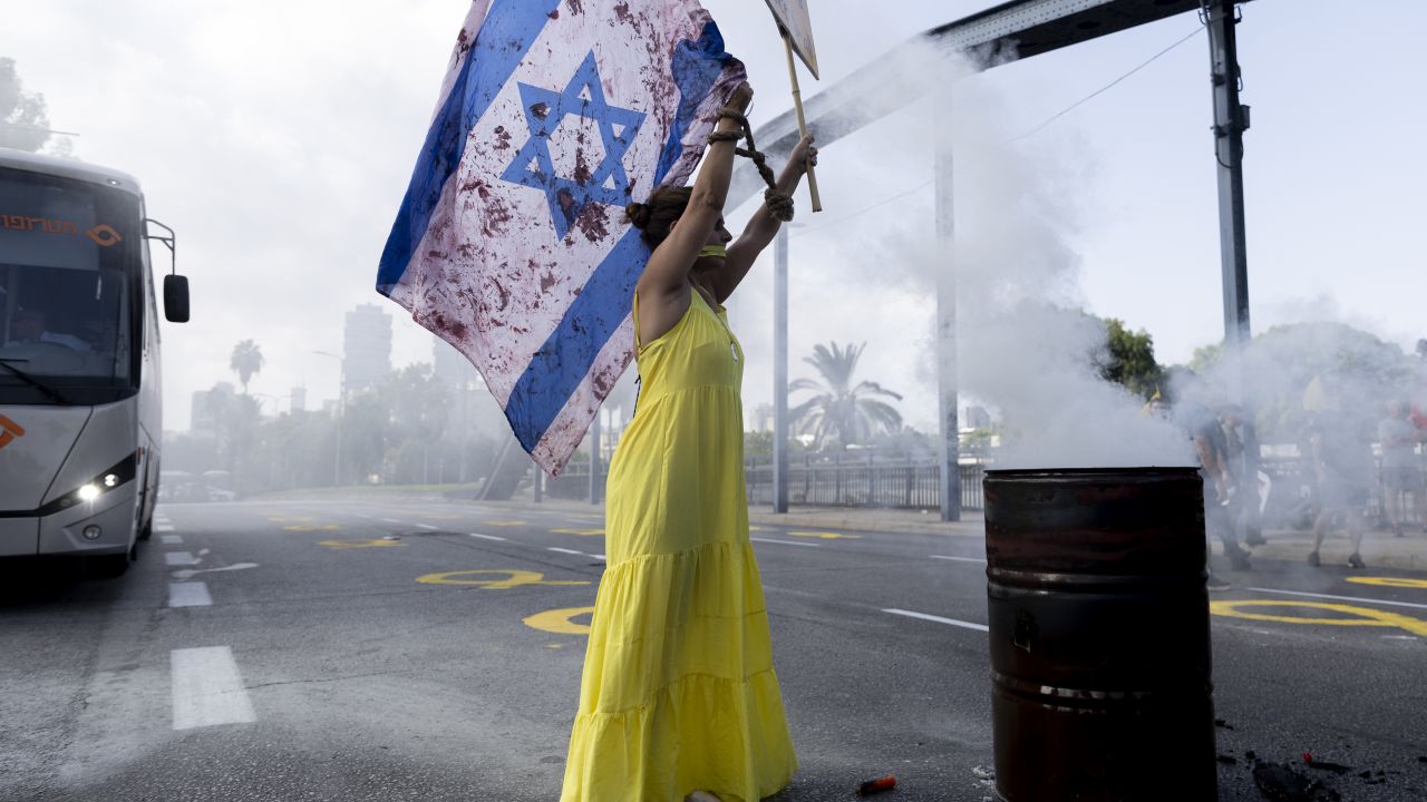 TEL AVIV, ISRAEL - SEPTEMBER 13: A woman holds an Israeli flag with red paint on to resemble blood as protesters block a main road during a rally calling for an hostages deal on September 13, 2024 in Tel Aviv, Israel. IDF released a footage from a tunnel in Gaza where six Israeli soldiers were held before executed by Hamas. (Photo by Amir Levy/Getty Images)