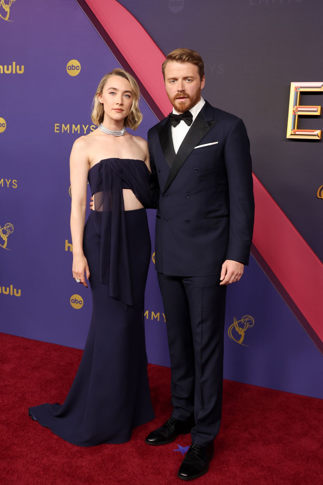 Saoirse Ronan llevaba un top drapeado de seda azul oscuro y una falda de corte A de seda doble de Louis Vuitton. El esmoquin de Jack Lowden también fue diseñado por la casa de lujo francesa.