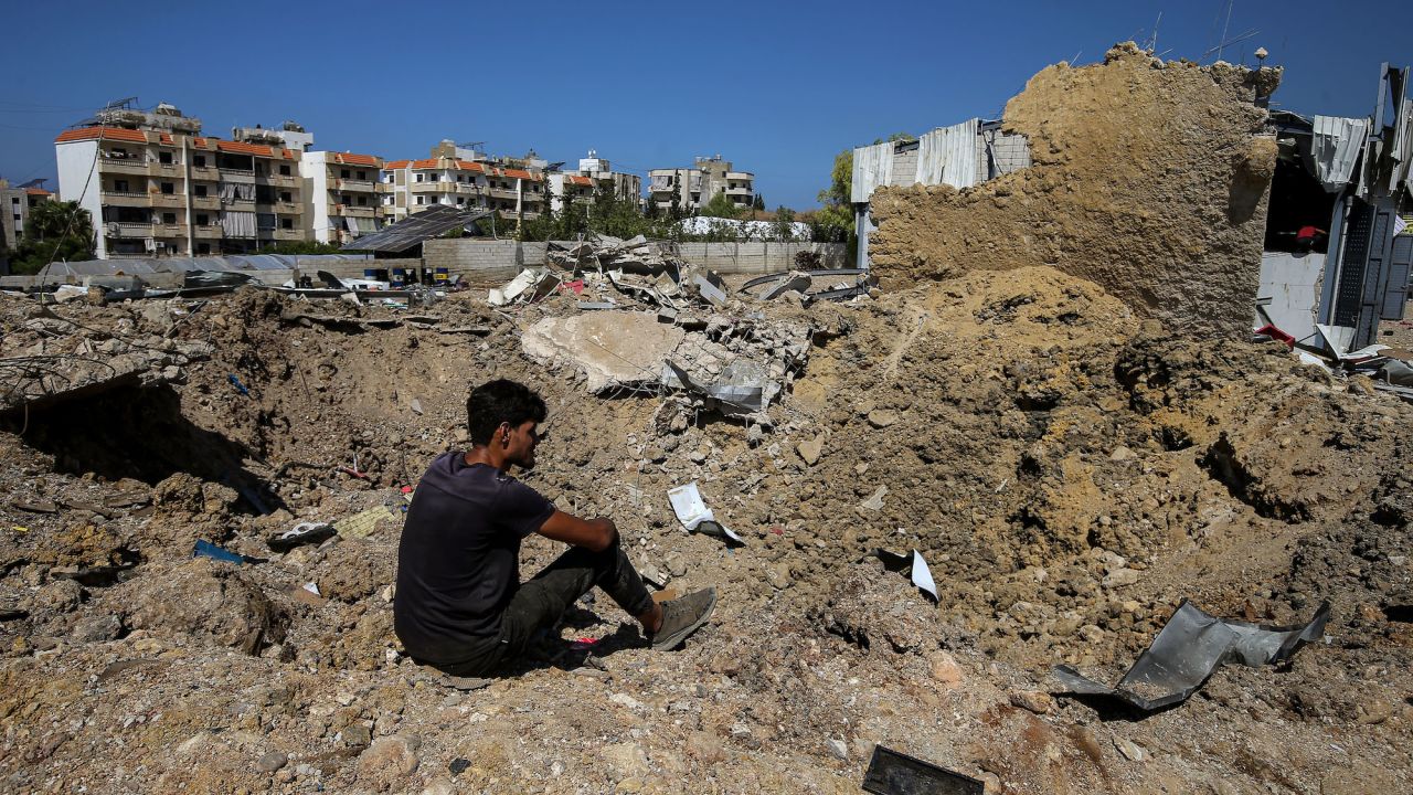 A man sits on the edge of a crater caused by an overnight Israeli air strike in the area of Jiyeh, Lebanon, on Wednesday.