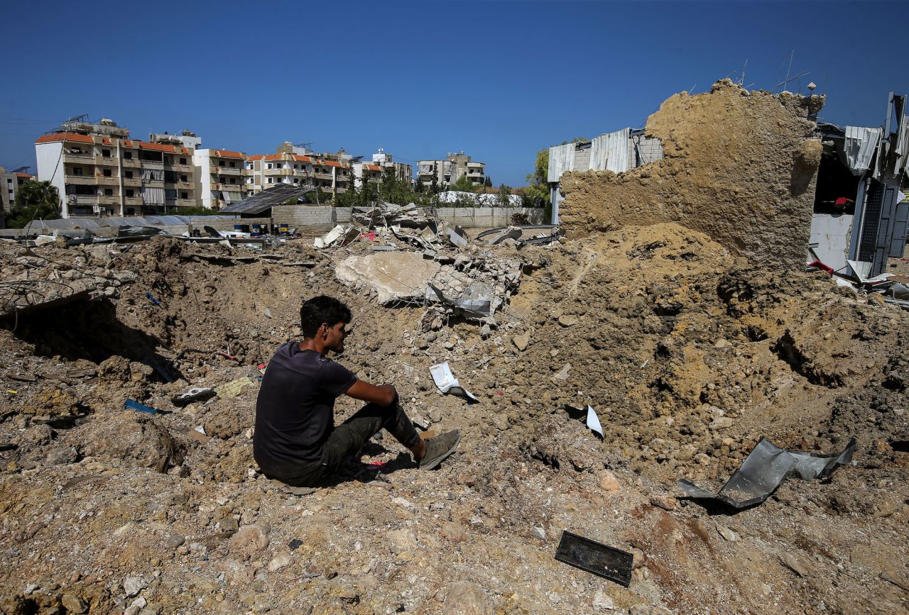 A man sits on the edge of a crater caused by an overnight Israeli air strike in the area of Jiyeh, Lebanon, on Wednesday.