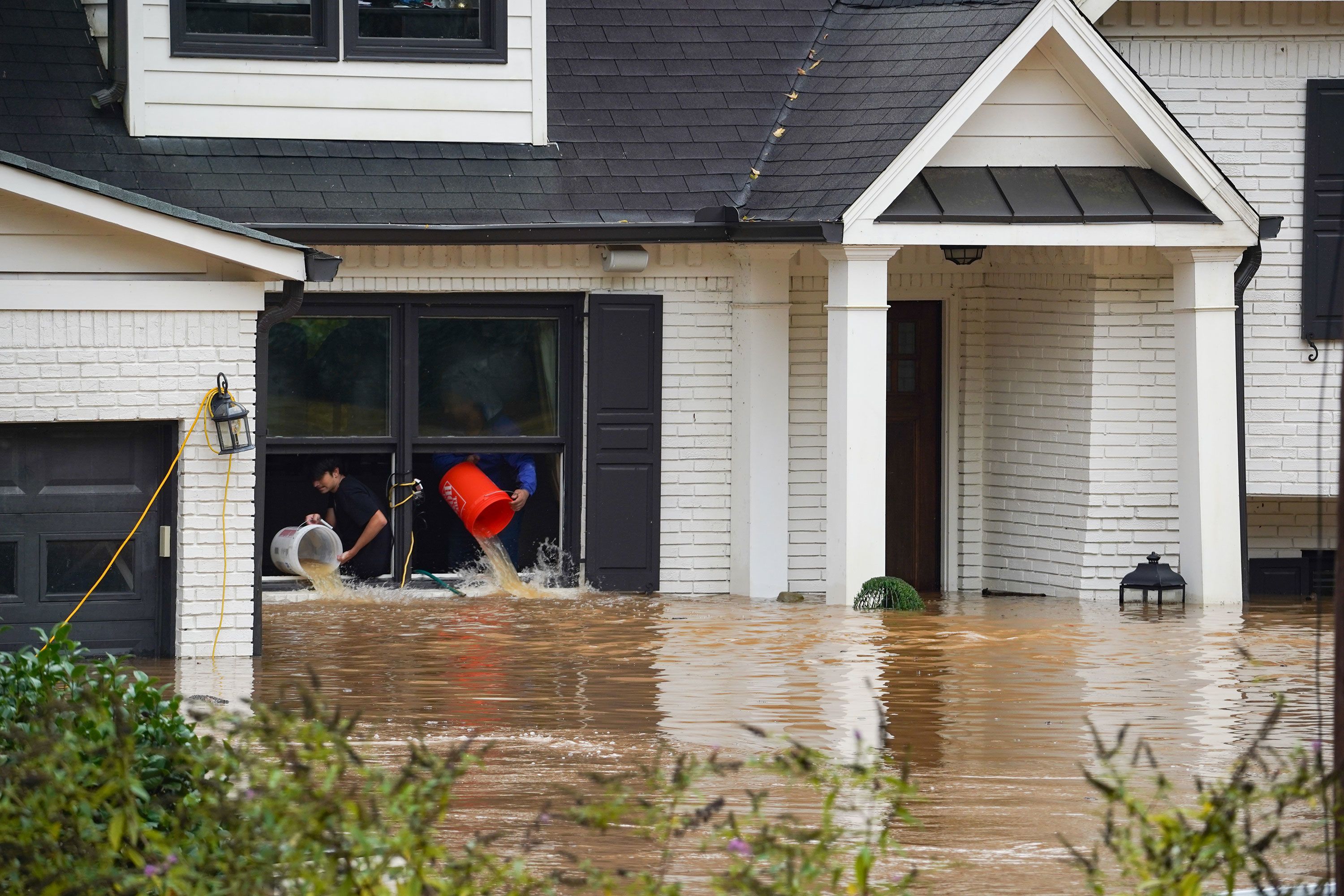 People using buckets to remove water from a home near Peachtree Creek in Atlanta after heavy rain from Hurricane Helene.