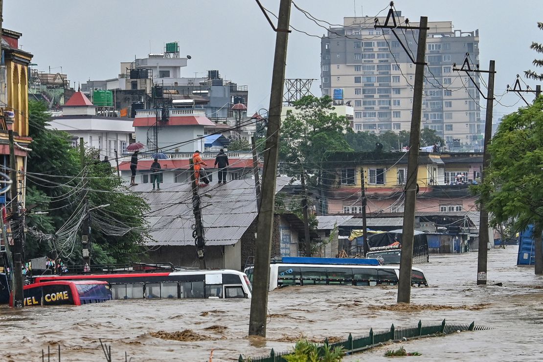 Residents climb over a rooftop as their neighborhood submerged in flood waters after the Bagmati River overflowed following heavy monsoon rains in Kathmandu on September 28, 2024.