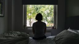 Powerful rear view shot of a mature woman looking out of her bedroom window - negative emotion - stock photo