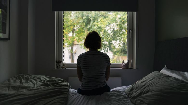 Powerful rear view shot of a mature woman looking out of her bedroom window - negative emotion - stock photo