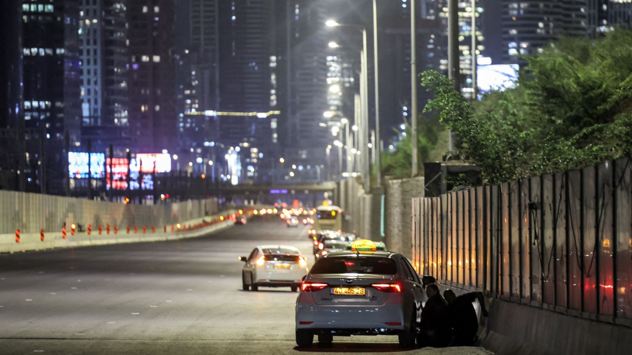 People take cover behind a vehicle parked along the side of a highway in Tel Aviv.