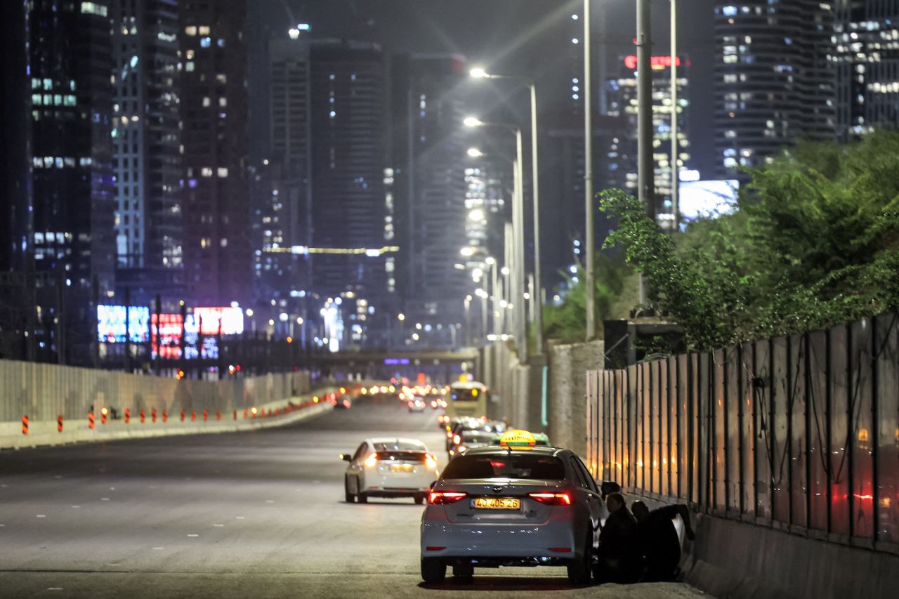 People take cover behind a vehicle parked along the side of a highway in Tel Aviv.