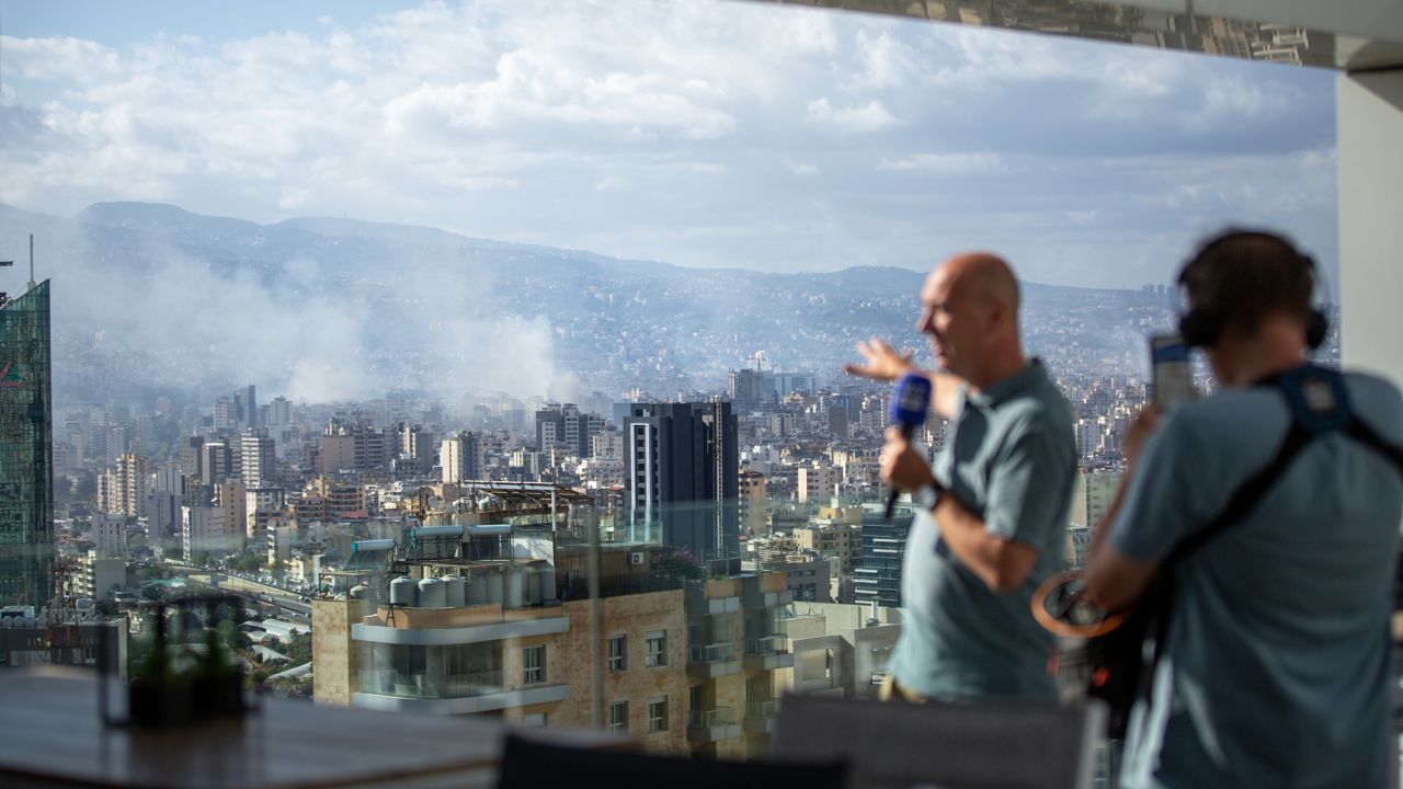 Broadcast journalists report as smoke rises from Israeli airstrikes that hit the city's southern suburbs early in the morning on October 2, in Beirut, Lebanon.