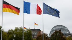 The flags of (L-R) Germany, France and the European Union fly in the wind in front of the Chancellery in Berlin, where the German Chancellor was expected to welcome the French President on October 2, 2024; in background can be seen the cupola of the Reichstag building that houses the Bundestag (lower house of parliament). (Photo by Ludovic MARIN / AFP) (Photo by LUDOVIC MARIN/AFP via Getty Images)