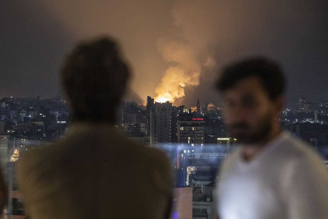 People take photos as smoke and flames rise following an Israeli airstrike on the Dahiyeh neighborhood early on Sunday.