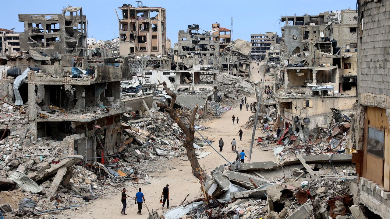 TOPSHOT - Palestinians walk on a dirt road lined with building rubble in the Shujaiya neighbourhood of Gaza City on October 7, 2024, on the first anniversary of the ongoing war in the Gaza Strip between Israel and the Palestinian Hamas group. (Photo by Omar AL-QATTAA / AFP) (Photo by OMAR AL-QATTAA/AFP via Getty Images)