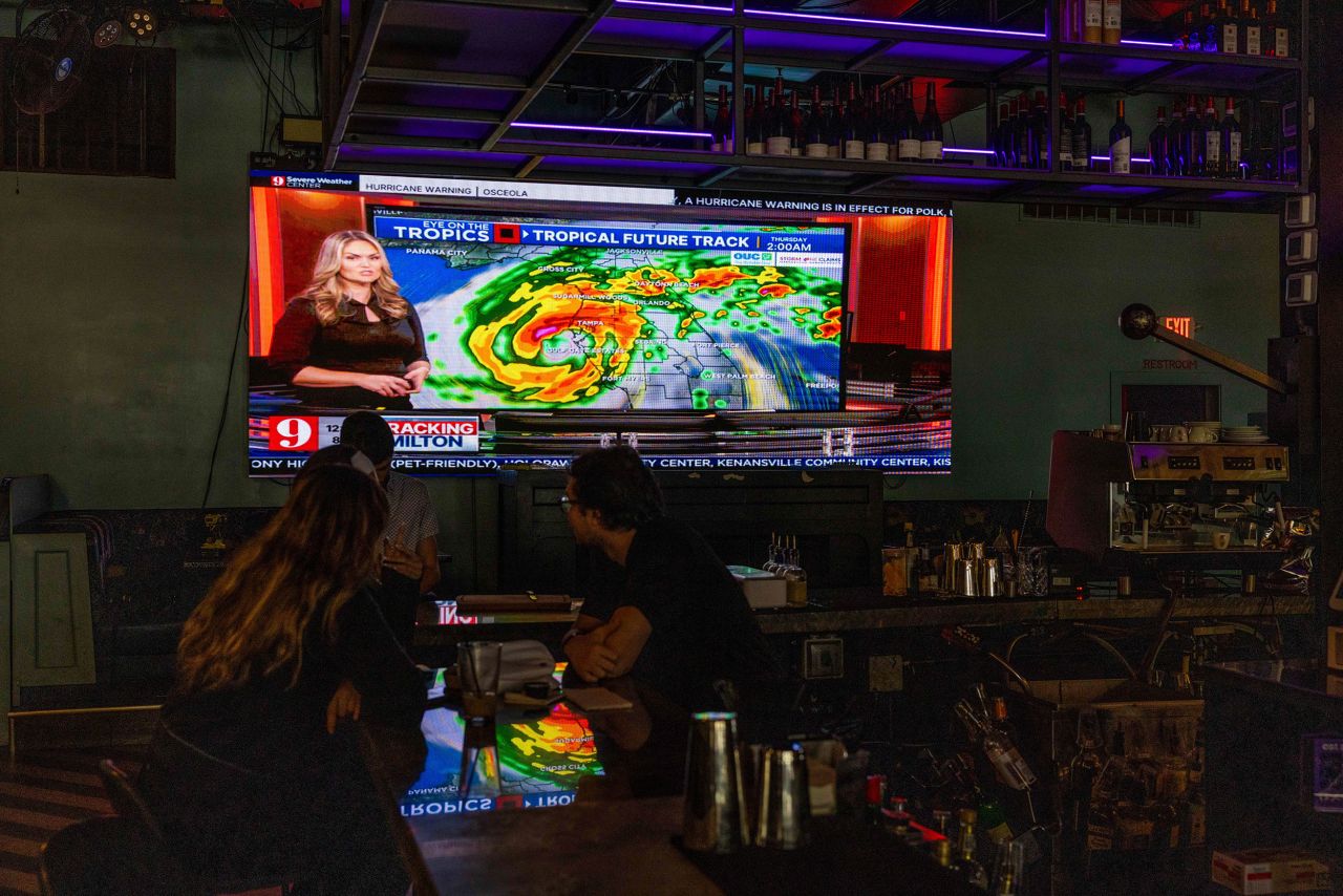 People watch a television screen at a bar showing the local news channel as the community prepares for Hurricane Milton on October 8 in Orlando, Florida.