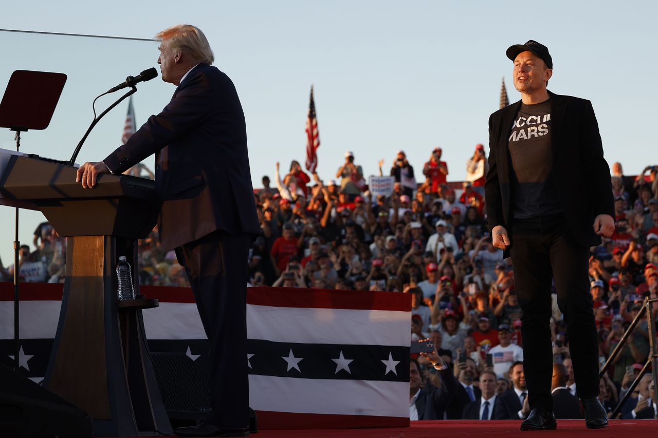 Elon Musk steps up onto the stage as former President Donald Trump addresses a campaign rally from behind bullet resistant glass at the Butler Farm Show fairgrounds on October 5, in Butler, Pennsylvania.