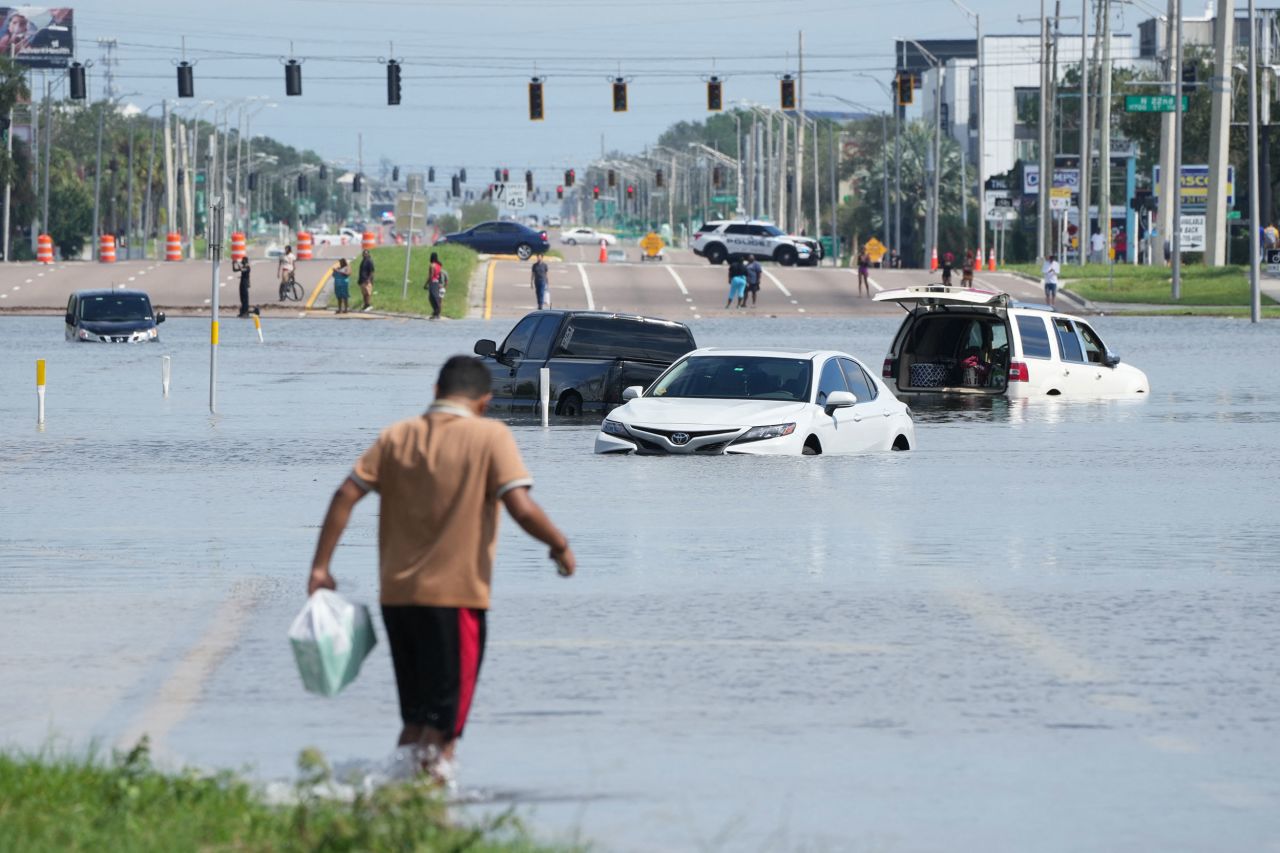 A man walks past flooded vehicles in Tampa, Florida, on Thursday.