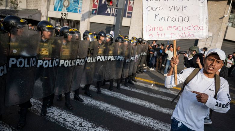 A member of the union of transporters and merchants holds a sign that reads in spanish 'We fight today to live tomorrow. Dina, listen to your people' in front of riot police during a protest against the wave of extortions in Lima on October 10, 2024. Dozens of transport workers and small traders held a protest march in Lima on Thursday, the second in less than two weeks against extortion and murder by organized crime. (Photo by Ernesto BENAVIDES / AFP) (Photo by ERNESTO BENAVIDES/AFP via Getty Images)