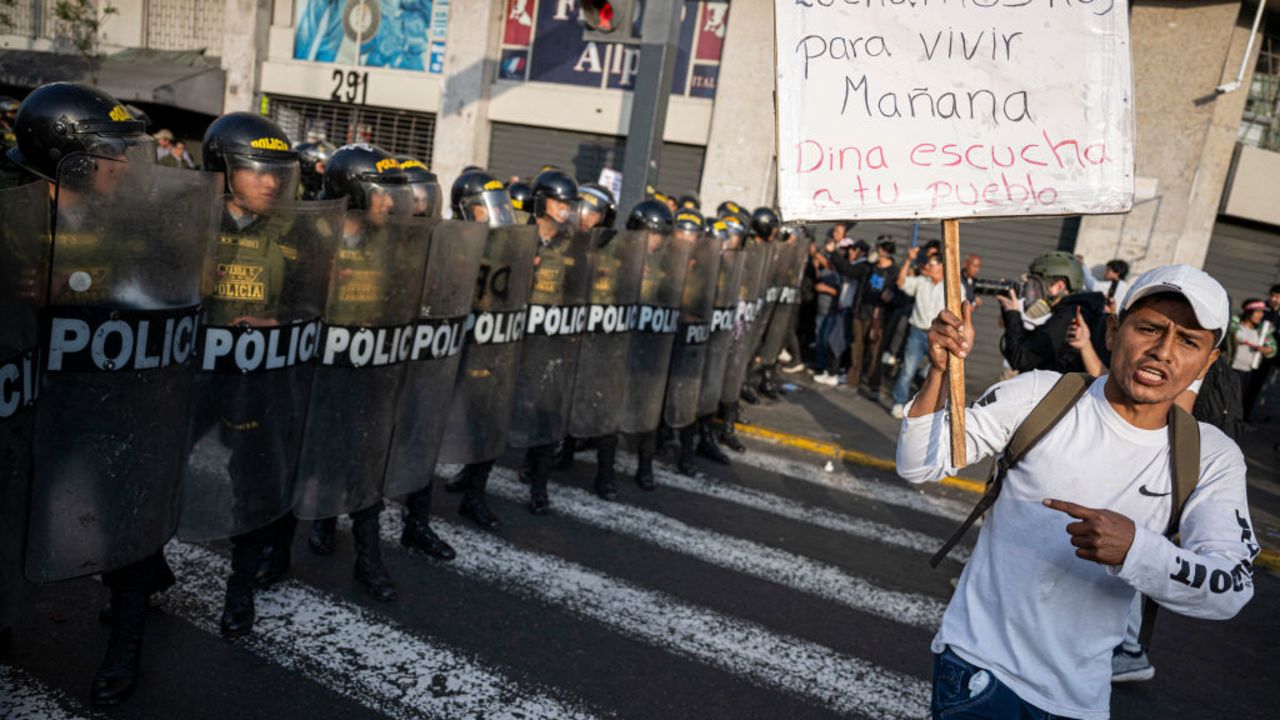 A member of the union of transporters and merchants holds a sign that reads in spanish 'We fight today to live tomorrow. Dina, listen to your people' in front of riot police during a protest against the wave of extortions in Lima on October 10, 2024. Dozens of transport workers and small traders held a protest march in Lima on Thursday, the second in less than two weeks against extortion and murder by organized crime. (Photo by Ernesto BENAVIDES / AFP) (Photo by ERNESTO BENAVIDES/AFP via Getty Images)