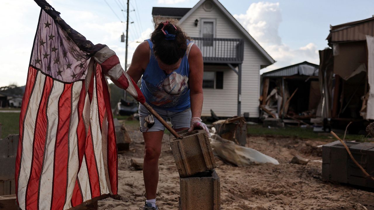 Roxanne Brooks mounts an American flag to a stack of cinderblocks outside her friend's destroyed mobile home (R) in the aftermath of Hurricane Helene flooding on October 6, 2024 in Swannanoa, North Carolina. Rescue and recovery efforts continue as the death toll has risen to over 230 in what is now the deadliest U.S. mainland hurricane since Katrina.