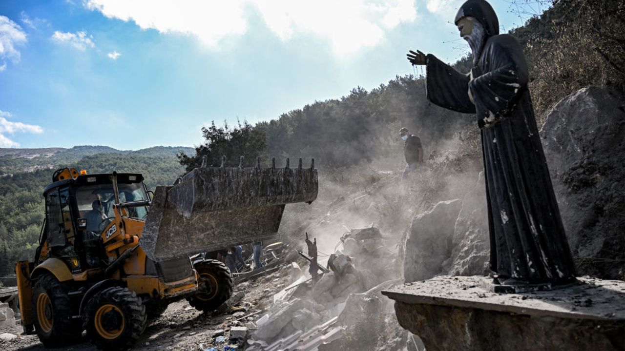 TOPSHOT - A Statue of the 19th-century Maronite Christian saint Mar Charbel is pictured as a bulldozer moves to clear rubble and debris from the site of a previous Israeli air strike on the village of Aito in northern Lebanon on October 15, 2024. The Lebanese Red Cross said at least 18 people died in a strike on north Lebanon on October 14, with the health ministry and official media reporting an Israeli raid on the Christian-majority area far from Hezbollah strongholds. (Photo by JOSEPH EID / AFP) (Photo by JOSEPH EID/AFP via Getty Images)