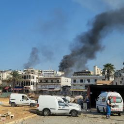 Rescuers at an emergency services center react as smoke billows during Israeli airstrikes in the southern Lebanese city of Nabatiyeh on October 16, 2024. A Lebanese official said Israel carried out 11 air strikes on Nabatiyeh and surrounding areas, days after strikes destroyed the southern city's marketplace. (Photo by Abbas Fakih / AFP) (Photo by ABBAS FAKIH/AFP via Getty Images)