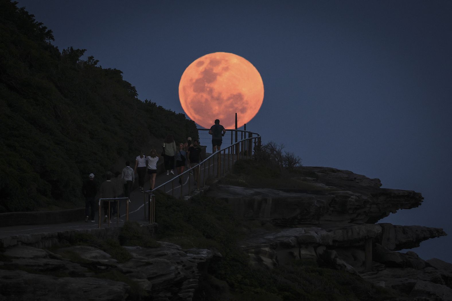 A super moon rises behind people walking on a headland near Sydney?s Bondi Beach on October 17, 2024. (Photo by DAVID GRAY / AFP) (Photo by DAVID GRAY/AFP via Getty Images)