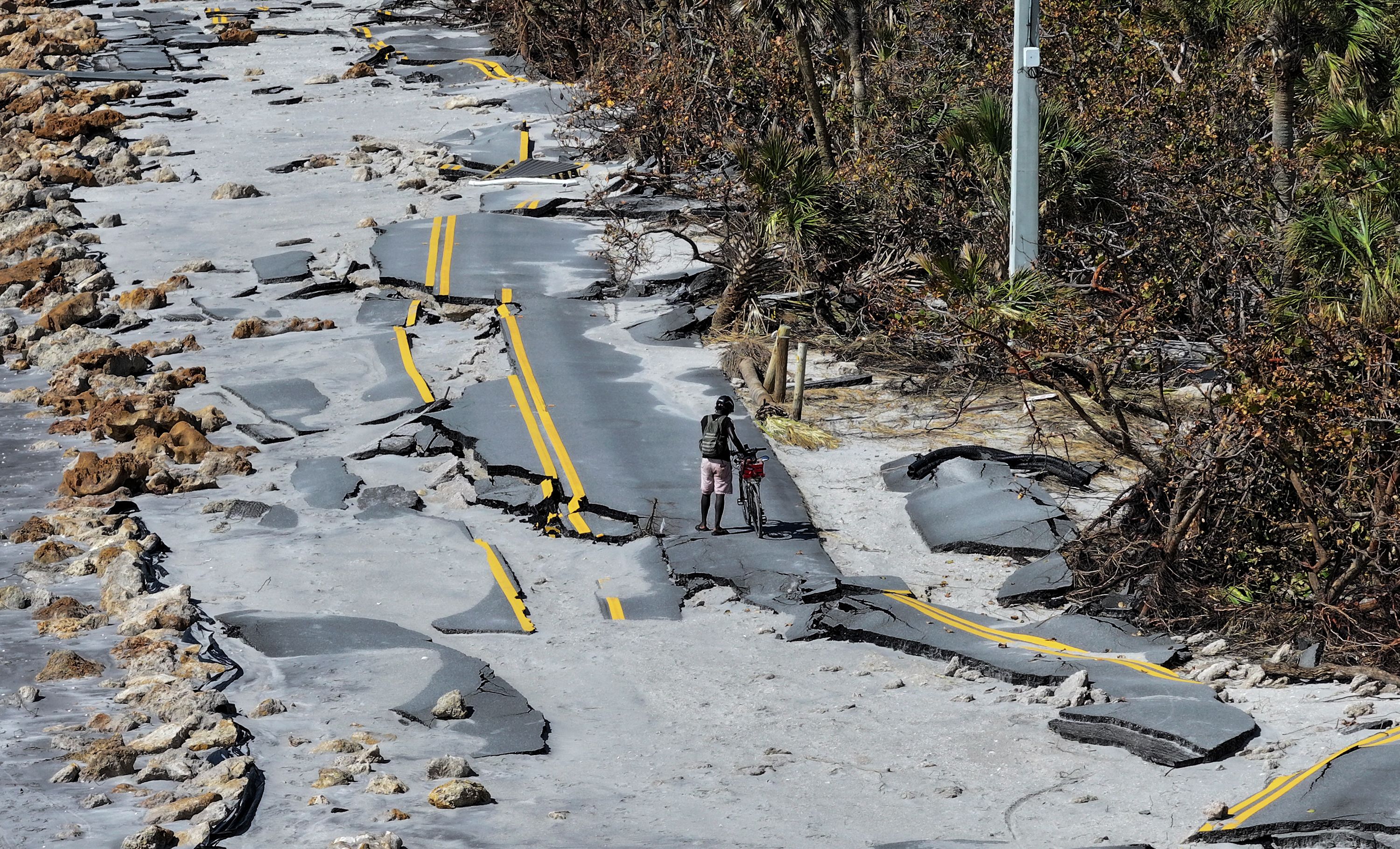 A bicycle rider navigates a damaged road along the Gulf of Mexico in Manasota Key, Florida, on Sunday, October 13.