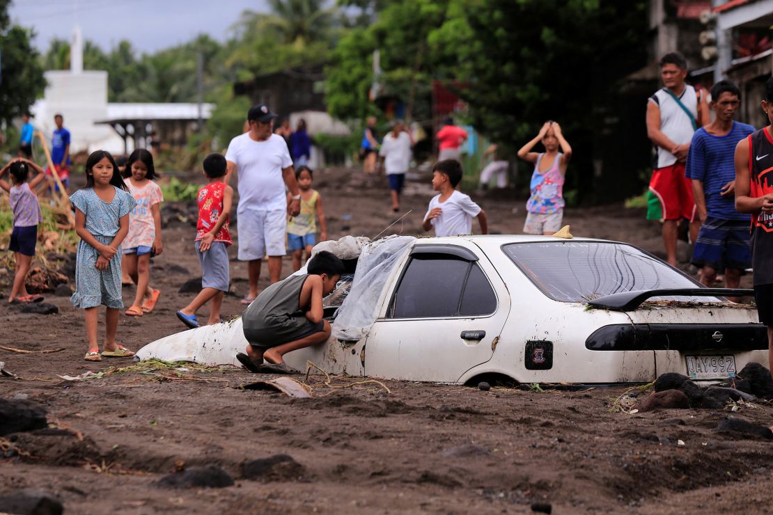 Residents look at a car buried by volcanic ash which cascaded into a village triggered by heavy rains brought about by Tropical Storm Trami at a village in Guinobatan town, Albay province south of Manila, Philippines, on October 23, 2024.