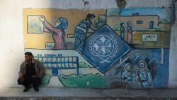 A man squats by a wall bearing a mural representing the UNRWA (United Nations Relief and Works Agency) at the aid agency's center at the Nuseirat camp for Palestinian refugees in the central Gaza Strip on October 29, 2024. Israel faced a mounting international backlash on October 29, after its parliament approved a bill banning the main UN aid agency for the devastated Gaza Strip. (Photo by Eyad BABA / AFP) (Photo by EYAD BABA/AFP via Getty Images)