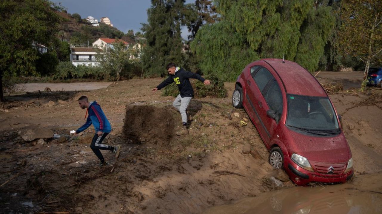 TOPSHOT - Men run next to a car covered with mud on a flooded street in Alora, near Malaga, on October 29, 2024, after a heavy rain hit southern Spain. (Photo by JORGE GUERRERO / AFP) (Photo by JORGE GUERRERO/AFP via Getty Images)