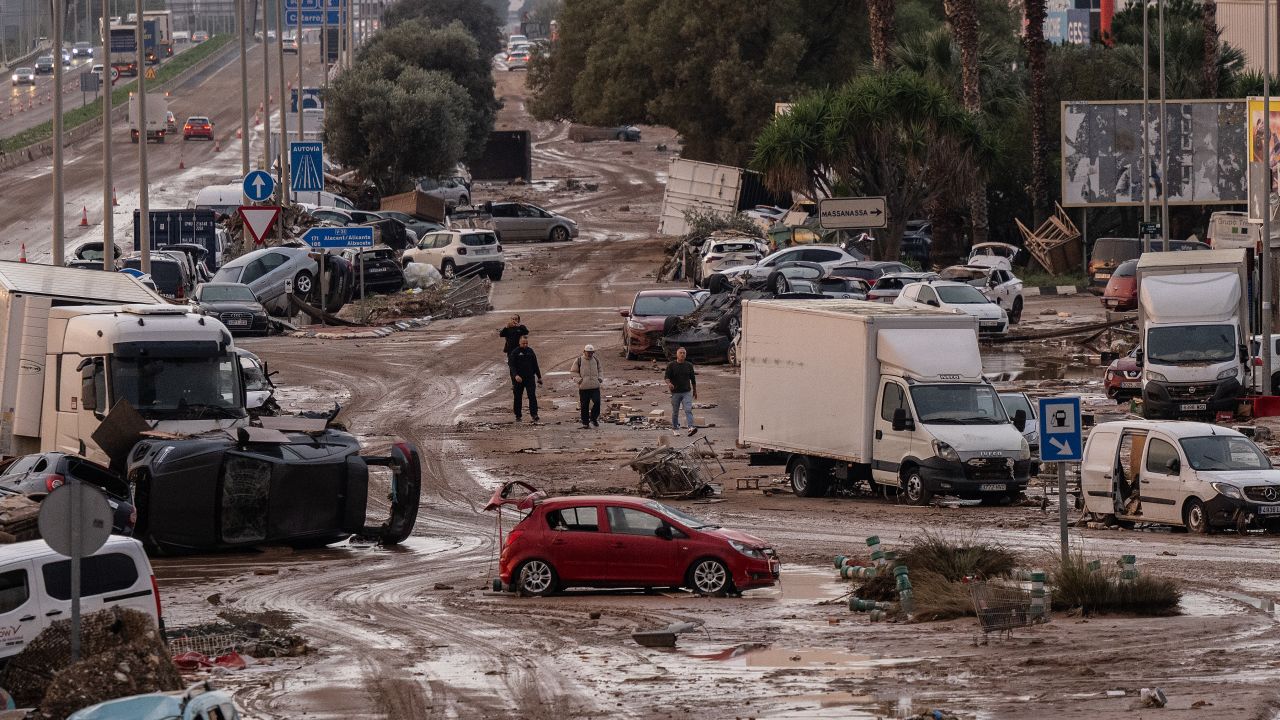 VALENCIA, SPAIN - NOVEMBER 1: People walk by cars and trucks that were among the debris swept up in recent flash flooding along the V-31 highway near the municipality of Massanassa on November 1, 2024 on the outskirts of Valencia, Spain. By Friday morning, Spanish authorities confirmed that at least 200 people had died, mostly in the Valencia region, amid the flooding that swept eastern and southern parts of the country starting on Tuesday. The intense rainfall event is known as a "cold drop" or DANA weather system. (Photo by David Ramos/Getty Images)