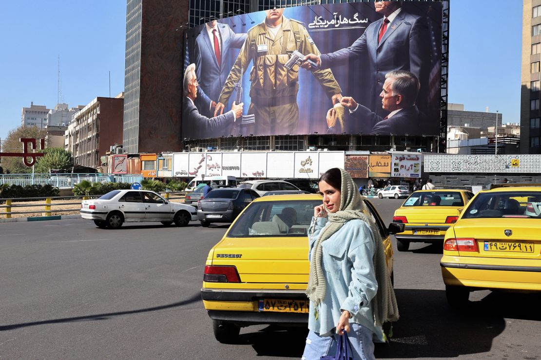 A woman crosses a road in front of an anti-Israel and US billboard depicting an Israeli soldier receiving military supplies from the United States with a Farsi headline reading 