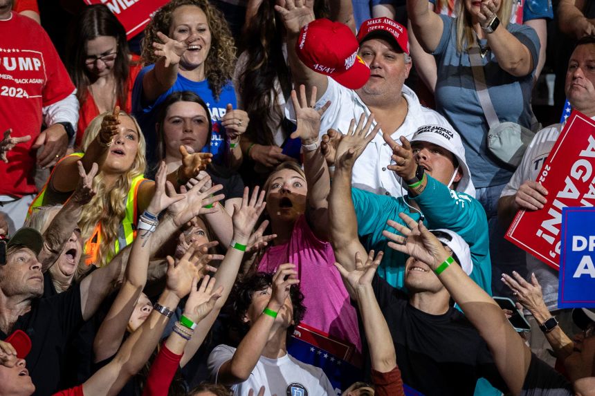Supporters of President Donald Trump reach for a thrown MAGA hat before a campaign rally in Macon, Georgia, on November 03, 2024.