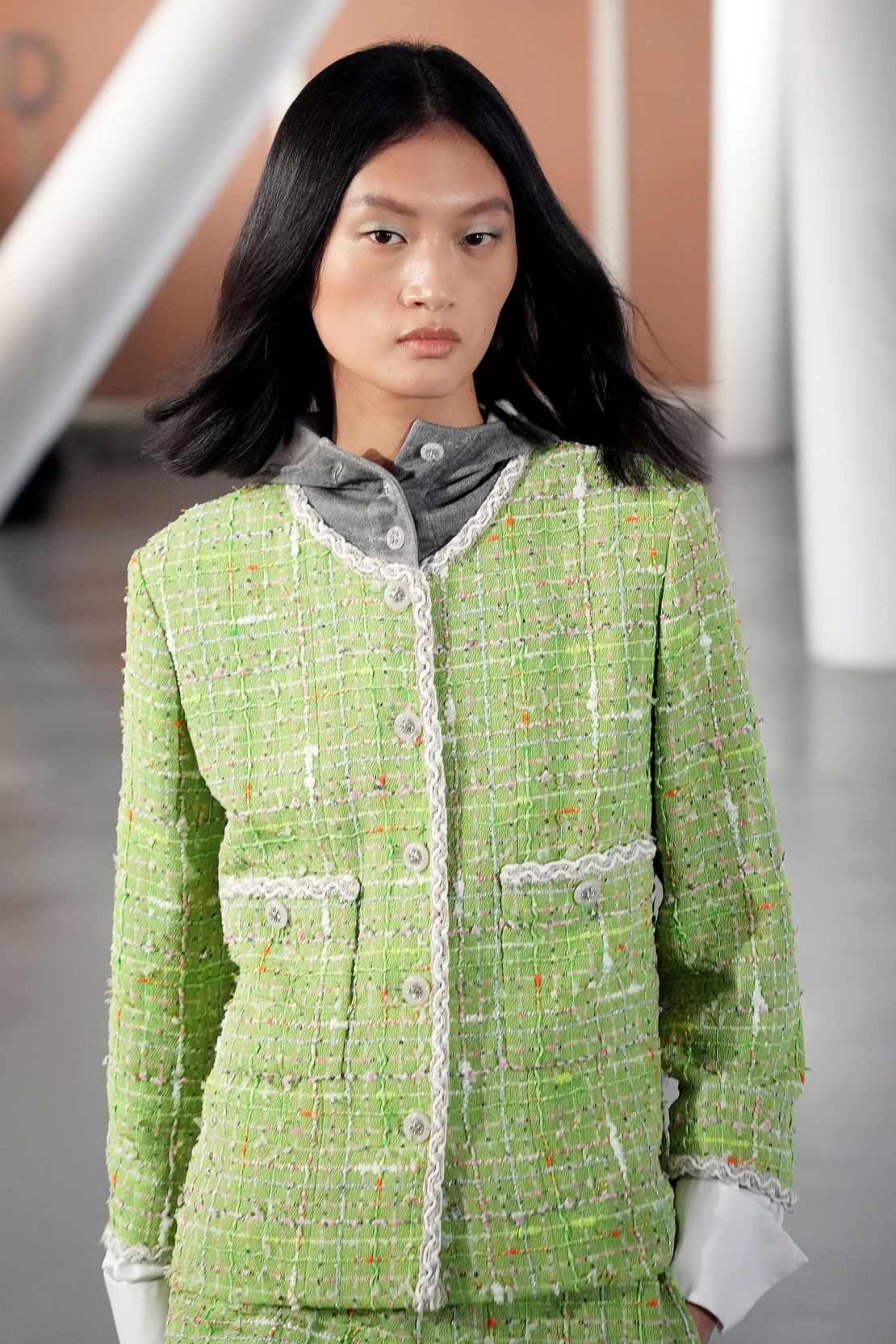 The show's opening look: a light green tweed jacket and skirt. A hooded grey sweatshirt underneath the ensemble gives a more relaxed feel.