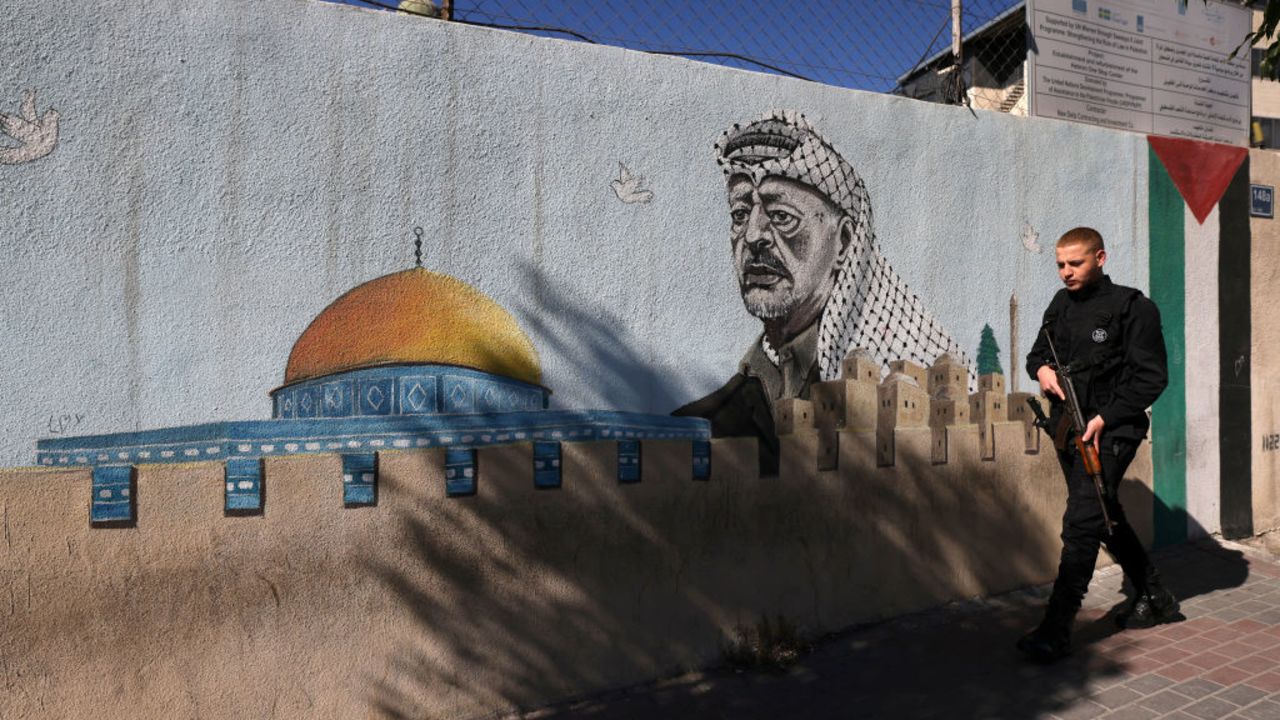 A Palestinian Authority policeman walks outside a police station adorned with a painting depicting late Palestinian leader Yasser Arafat, in the West Bank city of Hebron, on November 11, 2024, during the 20th anniversary of Arafat's death, amid increased violence in Israeli-occupied Palestinian territory as the war between Israel and the Hamas movement continues in the Gaza Strip. (Photo by HAZEM BADER / AFP) (Photo by HAZEM BADER/AFP via Getty Images)