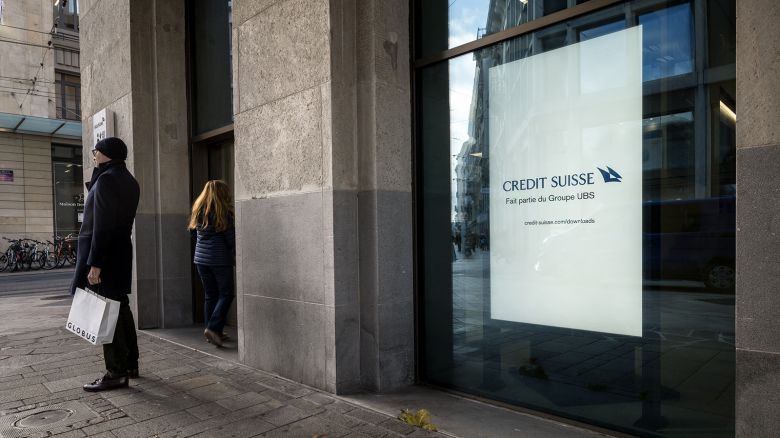 Poeple stand next to an advertising reading in French "Credit Suisse, part of UBS Group, in a showcase of a branch of Swiss banking Credit Suisse, absorbed last year by its ex-rival UBS, in Geneva, on November 14, 2024.
