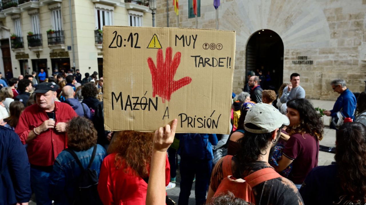 A person raises a sign reading "20:12 (warning) very late! Mazon to prison" as dozens of protesters gather outside the Valencia regional parliament, jeering and chanting slogans demanding the resignation of regional president Carlos Mazon, in Valencia on November 15, 2024. The head of Spain's eastern Valencia region admitted tday to "mistakes" in handling the country's deadliest flood in decades that killed 216 people there. "I'm not going to deny  mistakes," Carlos Mazon told the regional parliament in an address, adding he was "not going to shirk any responsibility". (Photo by JOSE JORDAN / AFP) (Photo by JOSE JORDAN/AFP via Getty Images)