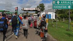 Members of the National Guard look at migrants of several nationalities bound to the Mexico-US border as they walk through Huehuetan, Chiapas State, Mexico on November 20, 2024. (Photo by ISAAC GUZMAN / AFP) (Photo by ISAAC GUZMAN/AFP via Getty Images)