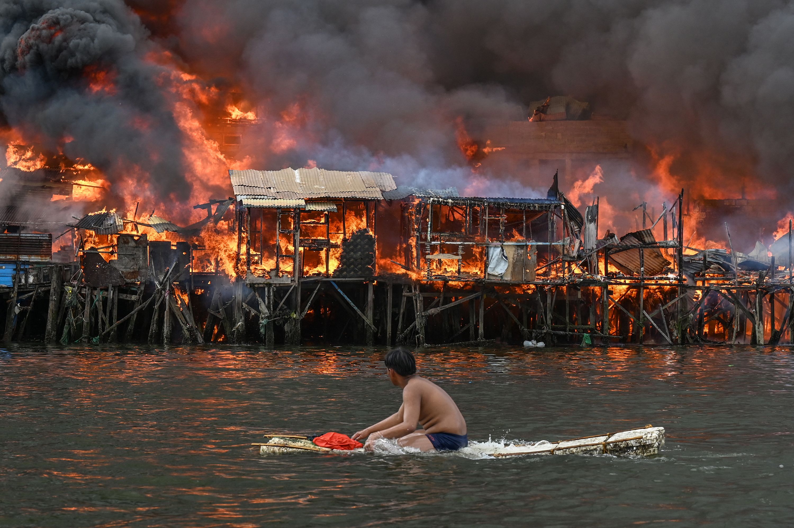 TOPSHOT - A man watches houses on fire at Tondo in Manila on November 24, 2024. Raging orange flames and thick black smoke billowed into the sky, as fire ripped through hundreds of houses in a closely built slum area of the Philippine capital Manila. (Photo by JAM STA ROSA / AFP) (Photo by JAM STA ROSA/AFP via Getty Images)