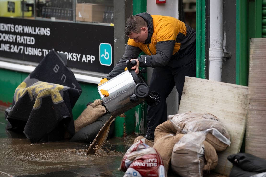 A man pours away water outside a flooded shop on Mill Street on November 24, 2024 in Pontypridd, Wales.