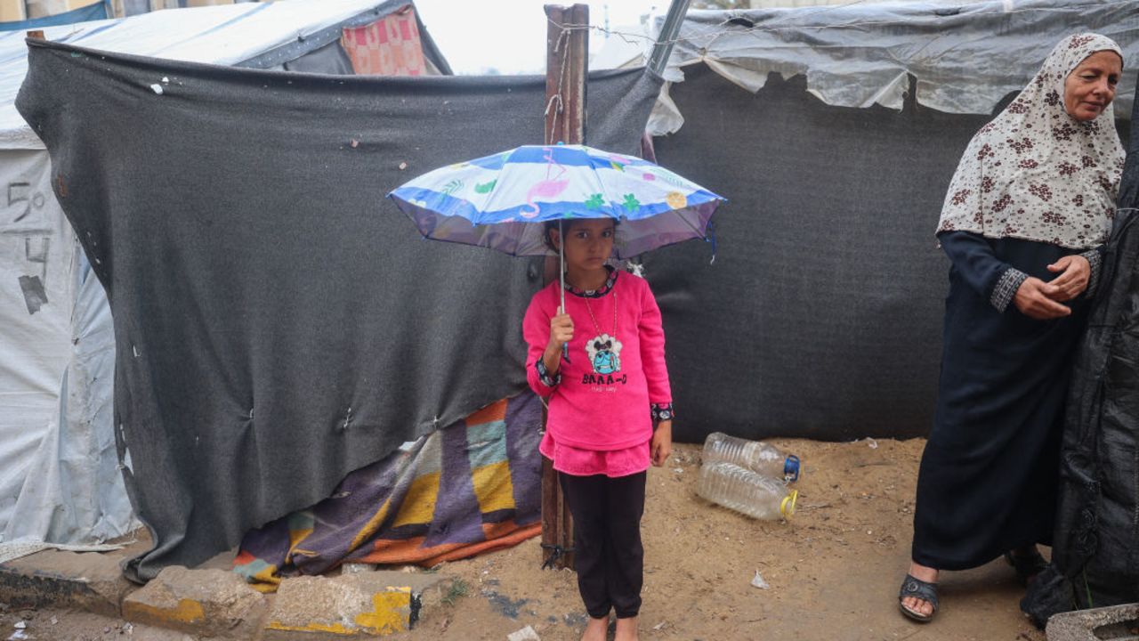 A barefoot Palestinian girl carries an umbrella to fend the rain next to displacement tents at the Bureij refugee camp in the central Gaza Strip on November 24, 2024, amid the ongoing war between Israel and the Palestinian Hamas militant group. (Photo by Eyad BABA / AFP) (Photo by EYAD BABA/AFP via Getty Images)