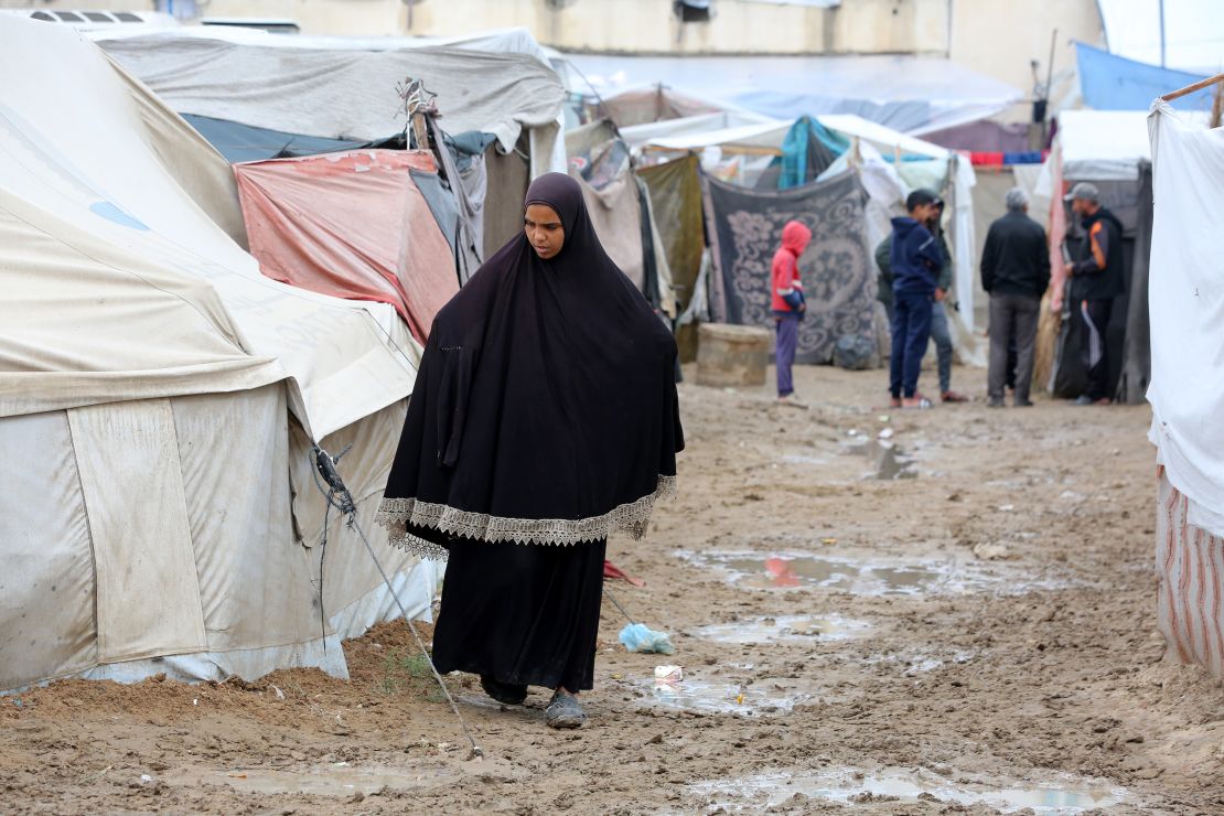 DEIR AL BALAH, GAZA - NOVEMBER 26: Palestinian woman living in makeshift tents walks between them, struggling with harsh weather conditions amid Israeli attacks in Deir al-Balah, Gaza, on November 26, 2024. Heavy rains have caused flooding in the tent camps, where thousands of people have taken shelter in the Gaza Strip. (Photo by Hassan Jedi/Anadolu via Getty Images)