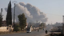Fighters enter the Rashidin district on the outskirts of Aleppo on their motorbikes with smoke billowing in the background during fighting on November 29, 2024, as Hayat Tahrir al-Sham (HTS) jihadists and allied factions continue their offensive in the Aleppo province against government forces. The jihadists along with Turkey-backed factions launched this week a shock offensive against Syrian regime troops and sparked the deadliest battle the country has seen in years, with the violence killing so far 242 people, according to the Syrian Observatory for Human Rights. The war monitor said most of the victims were combatants on both sides but also including civilians. (Photo by Bakr ALKASEM / AFP) (Photo by BAKR ALKASEM/AFP via Getty Images)