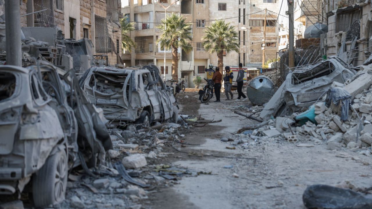 People and Syrian rescuers known as the White Helmets stand near building rubble at the site of a reported airstrike on a neighbourhood in Syria's rebel-held northern city of Idlib on December 2, 2024. (Photo by OMAR HAJ KADOUR / AFP) (Photo by OMAR HAJ KADOUR/AFP via Getty Images)