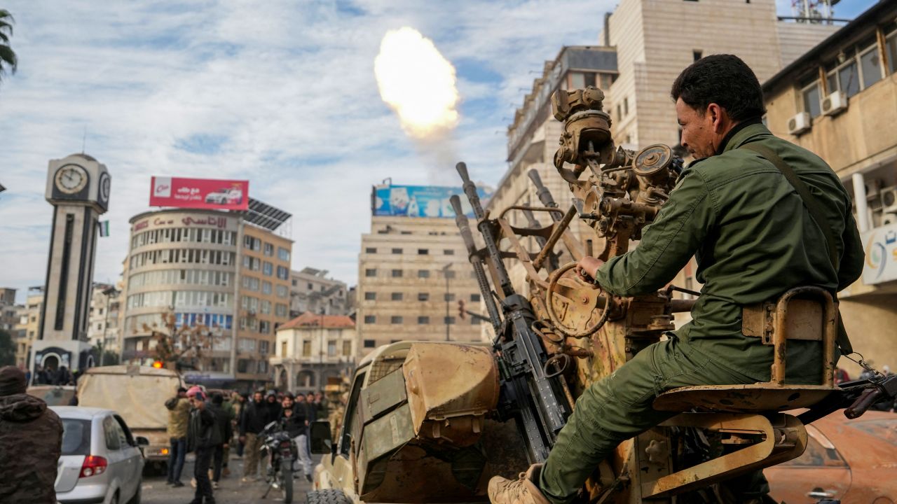 TOPSHOT - A Syrian rebel fighter fires rounds as people celebrate near the Clock Tower in the central city of Homs on December 8, 2024, after rebel forces entered Syria's third city overnight. Islamist-led rebels declared that they have taken Damascus in a lightning offensive on December 8, sending President Bashar al-Assad fleeing and ending five decades of Baath rule in Syria. (Photo by MUHAMMAD HAJ KADOUR / AFP) (Photo by MUHAMMAD HAJ KADOUR/AFP via Getty Images)