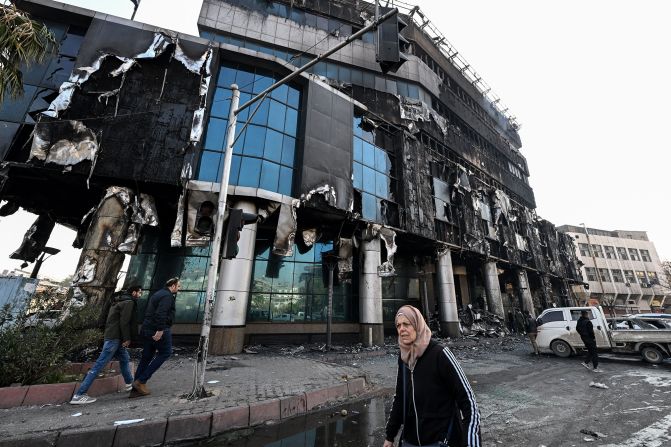 A woman walks past a heavily damaged Syrian government building, in Damascus, on December 9.