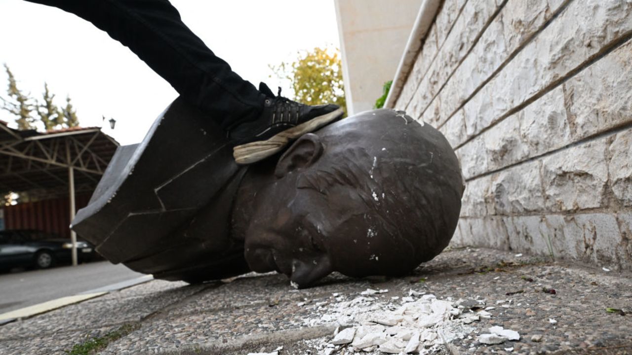 An anti-government fighter steps on the head of a statue of late Syrian president Hafez al-Assad that was brought down outside the Defence Ministry's military security headquarters in the Damascus district of Kafr Sousa on December 9, 2024. Syrians flocked to the main square of the capital city Damascus on December 9 to mark what many regard as a long-awaited new dawn after the fall of president Bashar al-Assad who's father and predecessor died in 2000. (Photo by LOUAI BESHARA / AFP) (Photo by LOUAI BESHARA/AFP via Getty Images)