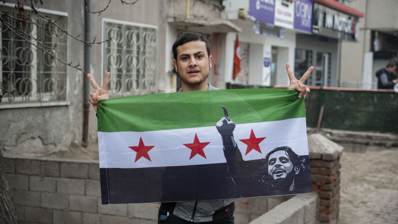 A man holds the Syrian opposition flag high while others join in chants during a rally in Turkey on December 8, 2024. The event signifies widespread celebration among Syrian expatriates over Assad's regime collapse. (Photo by Damoun Pournemati / Middle East Images / Middle East Images via AFP) (Photo by DAMOUN POURNEMATI/Middle East Images/AFP via Getty Images)