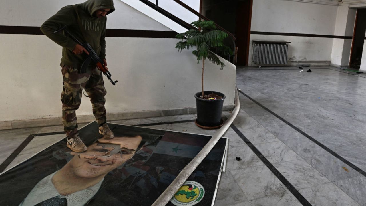 A rebel fighter steps on a defaced portrait of toppled Syrian president Bashar al-Assad during a raid at the Baath party offices in Damascus, on December 12, 2024. Islamist-led rebels took Damascus in a lightning offensive on December 8, ousting Assad and ending five decades of Baath rule in Syria. (Photo by LOUAI BESHARA / AFP) (Photo by LOUAI BESHARA/AFP via Getty Images)