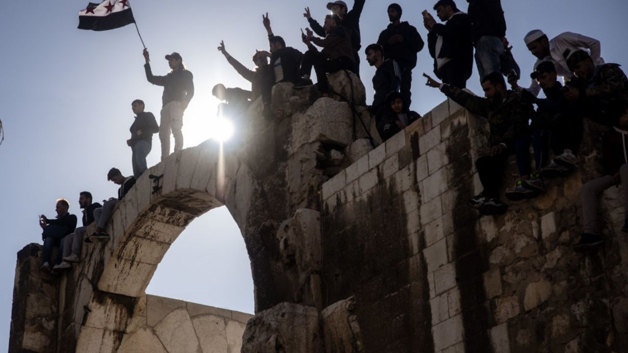 DAMASCUS, SYRIA - DECEMBER 13: People wave flags in celebration while standing on an old city wall after thousands of people participated in the first Friday prayer since the fall of the Assad regime outside the Umayyad Mosque on December 13, 2024 in Damascus, Syria. Rebel forces in Syria have retaken the capital from longtime ruler Bashar al-Assad, who has fled the country for Moscow. The fall of the Assad regime marks a new chapter for Syria, which has been mired in a multi-party civil war since 2011, sparked by the Arab Spring uprisings. (Photo by Chris McGrath/Getty Images)