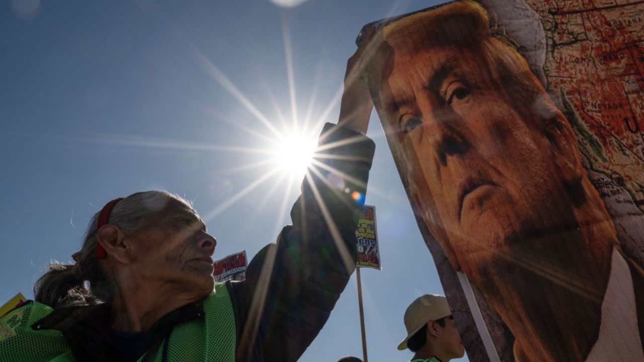 TOPSHOT - A demonstrator holds a banner with the image of US President-elect Donald Trump as she protests at the San Ysidro crossing port on the US-Mexico border in Tijuana, Baja California State, Mexico, on December 18, 2024, during International Migrants Day. (Photo by Guillermo Arias / AFP) (Photo by GUILLERMO ARIAS/AFP via Getty Images)