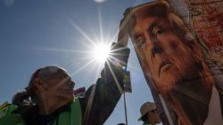 TOPSHOT - A demonstrator holds a banner with the image of US President-elect Donald Trump as she protests at the San Ysidro crossing port on the US-Mexico border in Tijuana, Baja California State, Mexico, on December 18, 2024, during International Migrants Day. (Photo by Guillermo Arias / AFP) (Photo by GUILLERMO ARIAS/AFP via Getty Images)