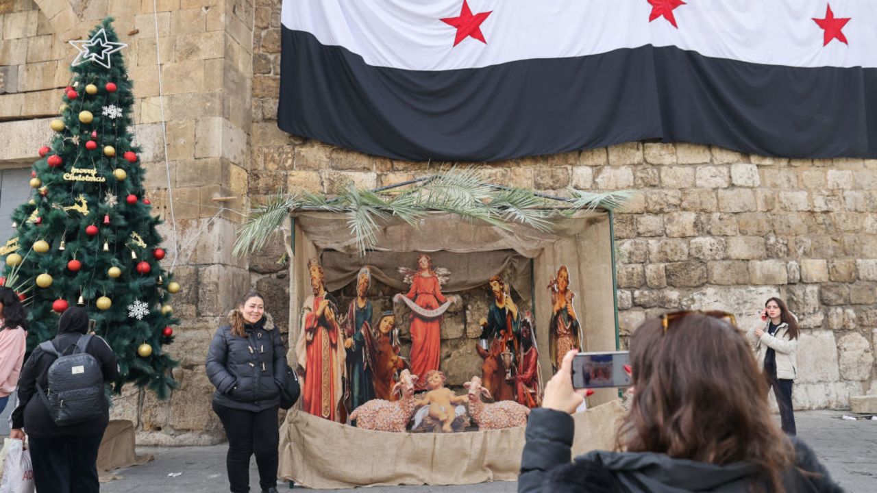 People pose for pictures with a Christmas manger set up beneath an independence-era Syrian flag in the Bab Touma neighbourhood of Damascus on December 23, 2024. (Photo by ANWAR AMRO / AFP) (Photo by ANWAR AMRO/AFP via Getty Images)